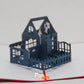 Closer picture of pop-up card showing large blue house with white Christmas tree in top floor living room