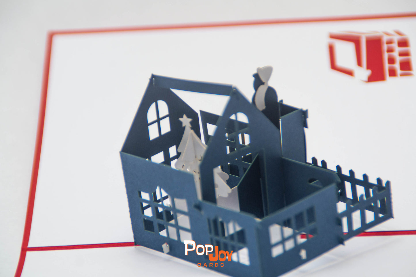 Top-view of pop-up card showing large blue house with white Christmas tree in top floor living room