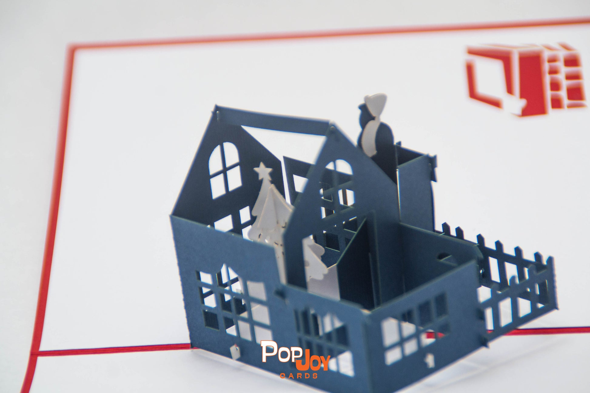 Top-view of pop-up card showing large blue house with white Christmas tree in top floor living room