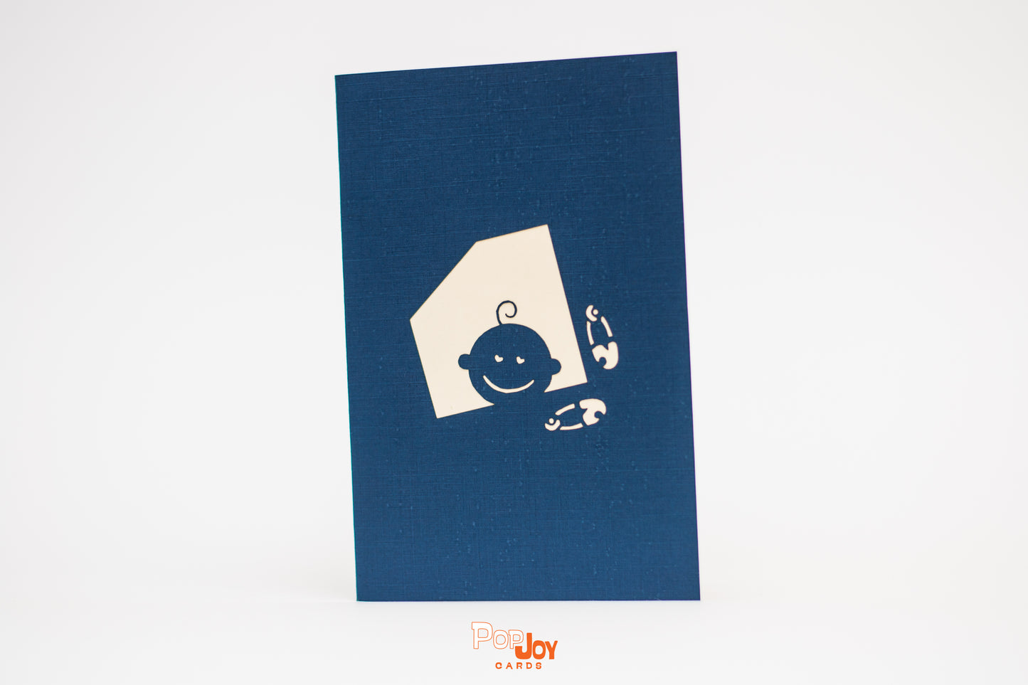 Dark blue card with silhouette of baby peeking out of window and two diaper pins on front cover