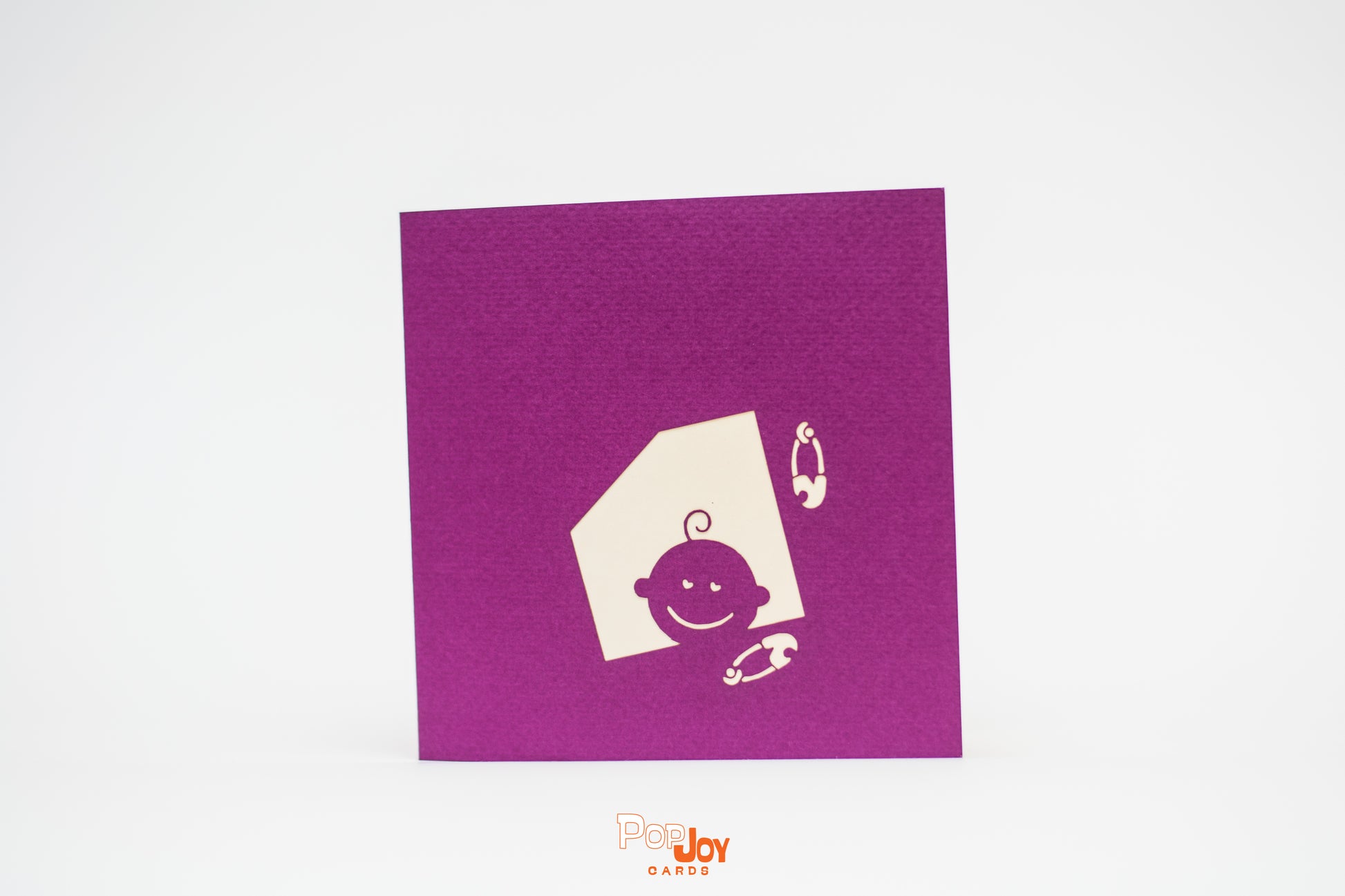 Purple card with silhouette of baby peeking out of window and two diaper pins on front cover