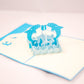 Pop-up card showing two blue dolphins playing with a ball in the middle, while surrounded by waves and other dolphins